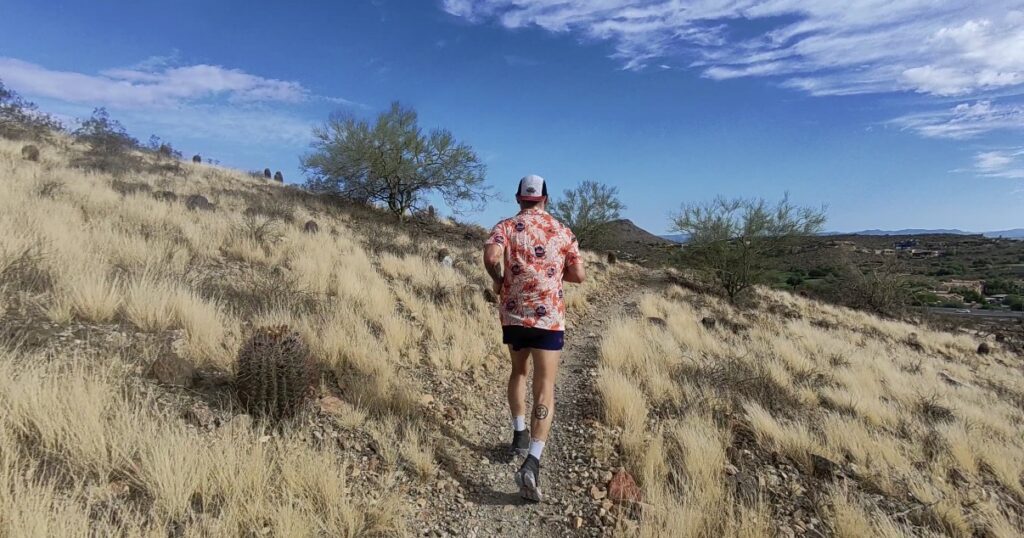 Jason Bahamundi running uphill on a rocky desert trail in Arizona.